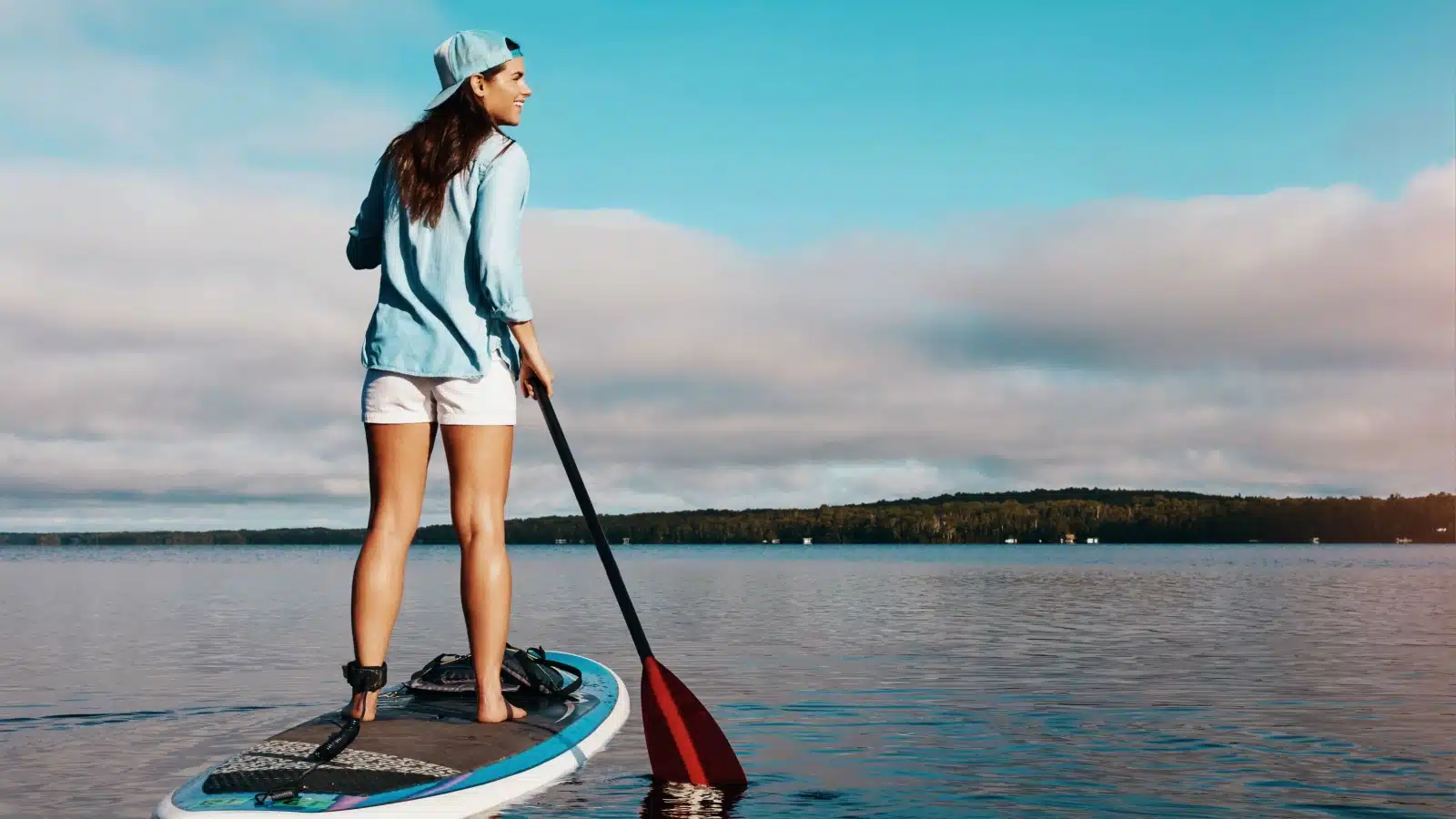 A woman paddle boards on a lake in the summer.