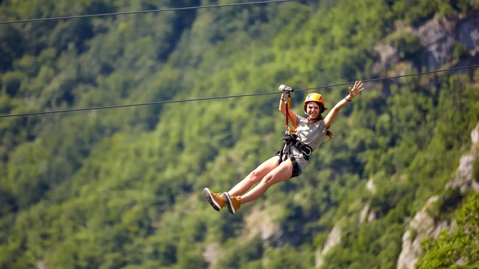 A woman waves as she rides a zipline.