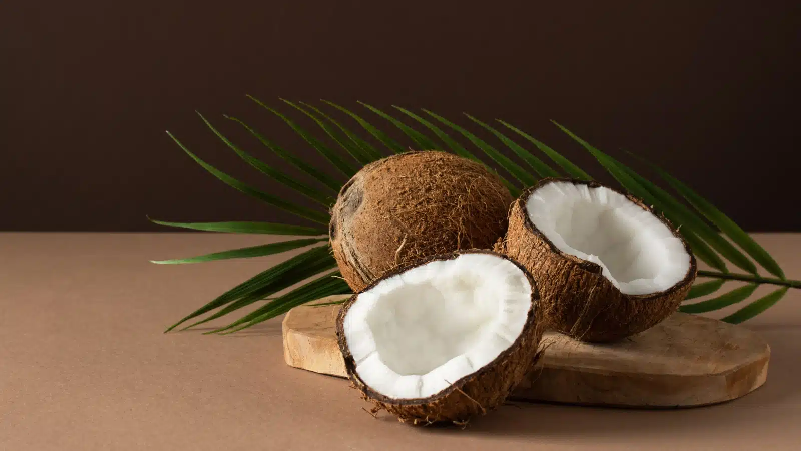 Coconuts on a cutting board with a palm leaf in the background.