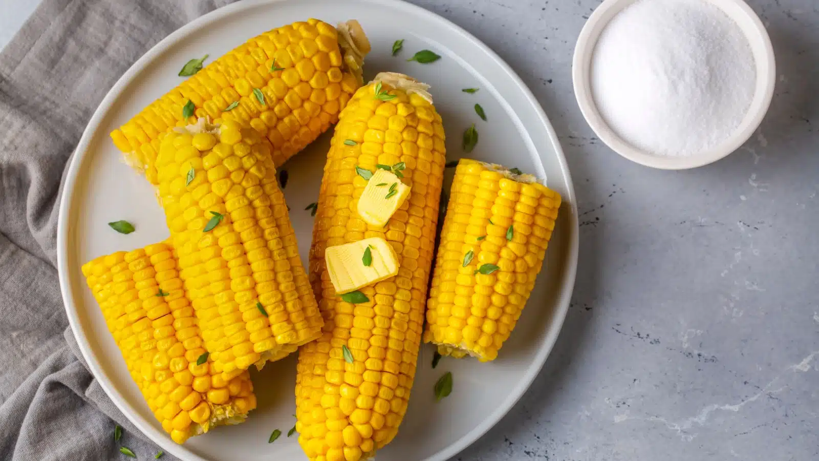 A plate of cooked corn on the cob with butter and salt.