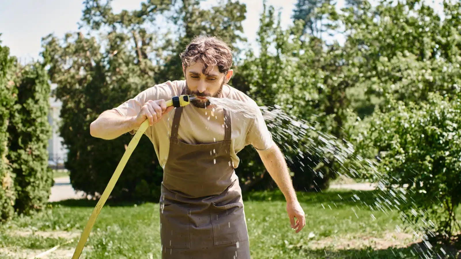 A man drinks from the hose while working in the garden.
