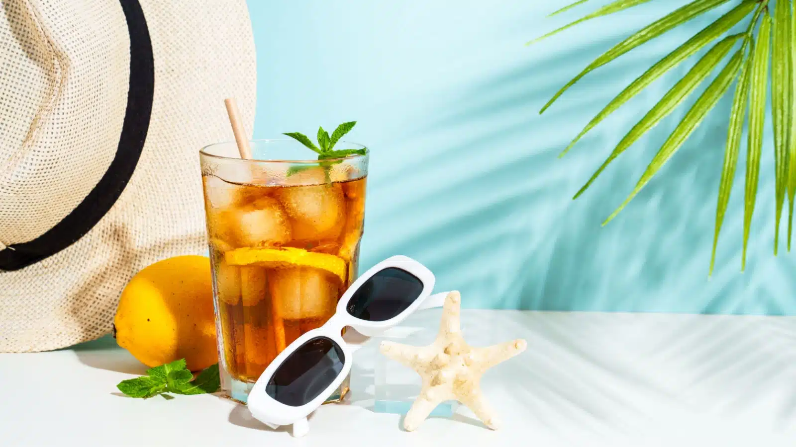 A refreshing looking iced tea rests with other summer and beach items, like a beach hat, sunglasses, and a starfish.