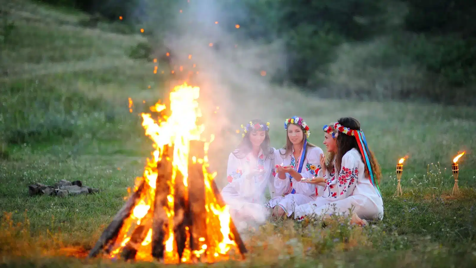 Girls in white with flower wreaths enjoy a bonfire during the midsummer celebration.