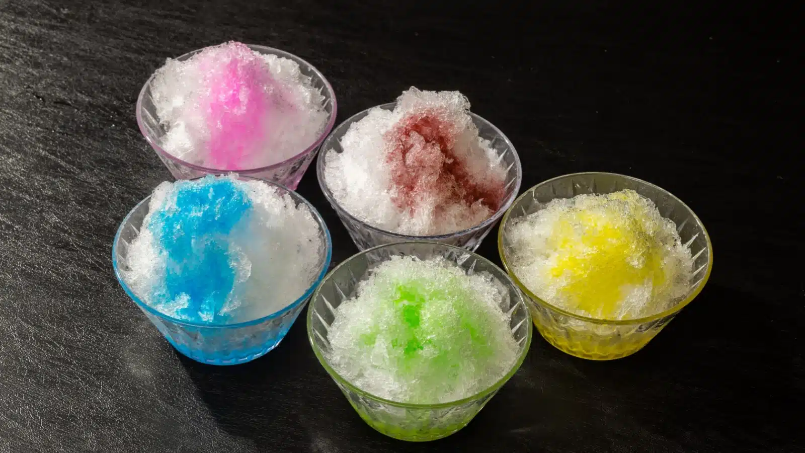 Five bowls of shaved ice with different flavor toppings.