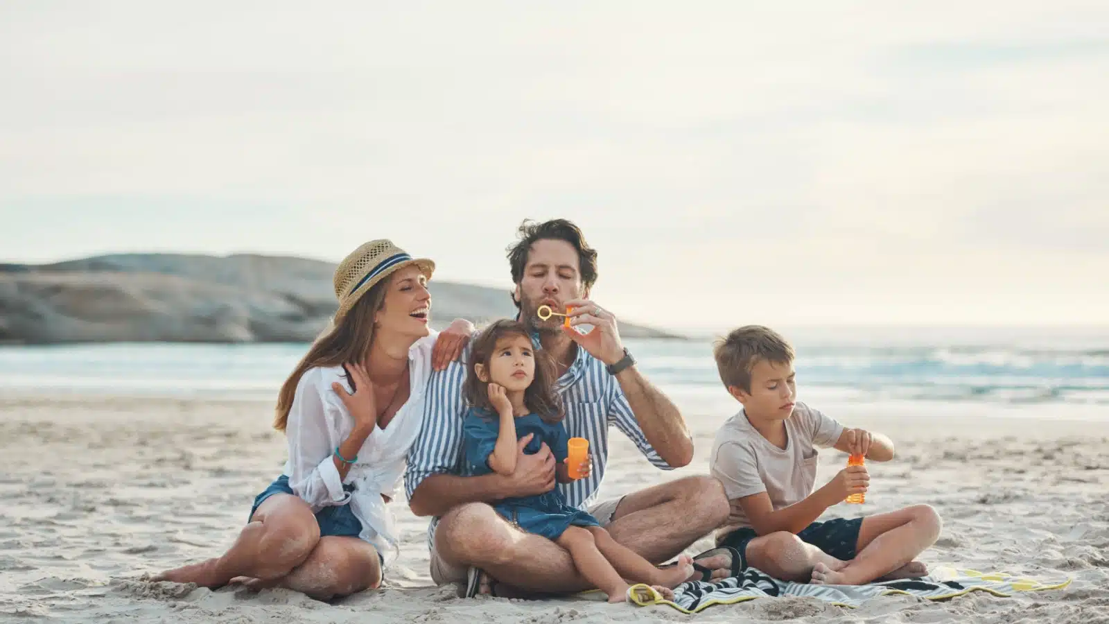 A happy family enjoys a day at the beach blowing bubbles.