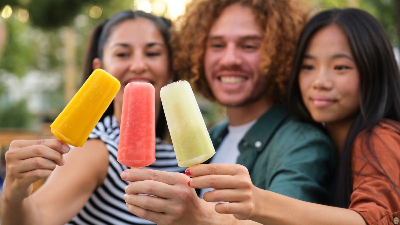 Friends holding out different colored popsicles to represent the best summer flavors.