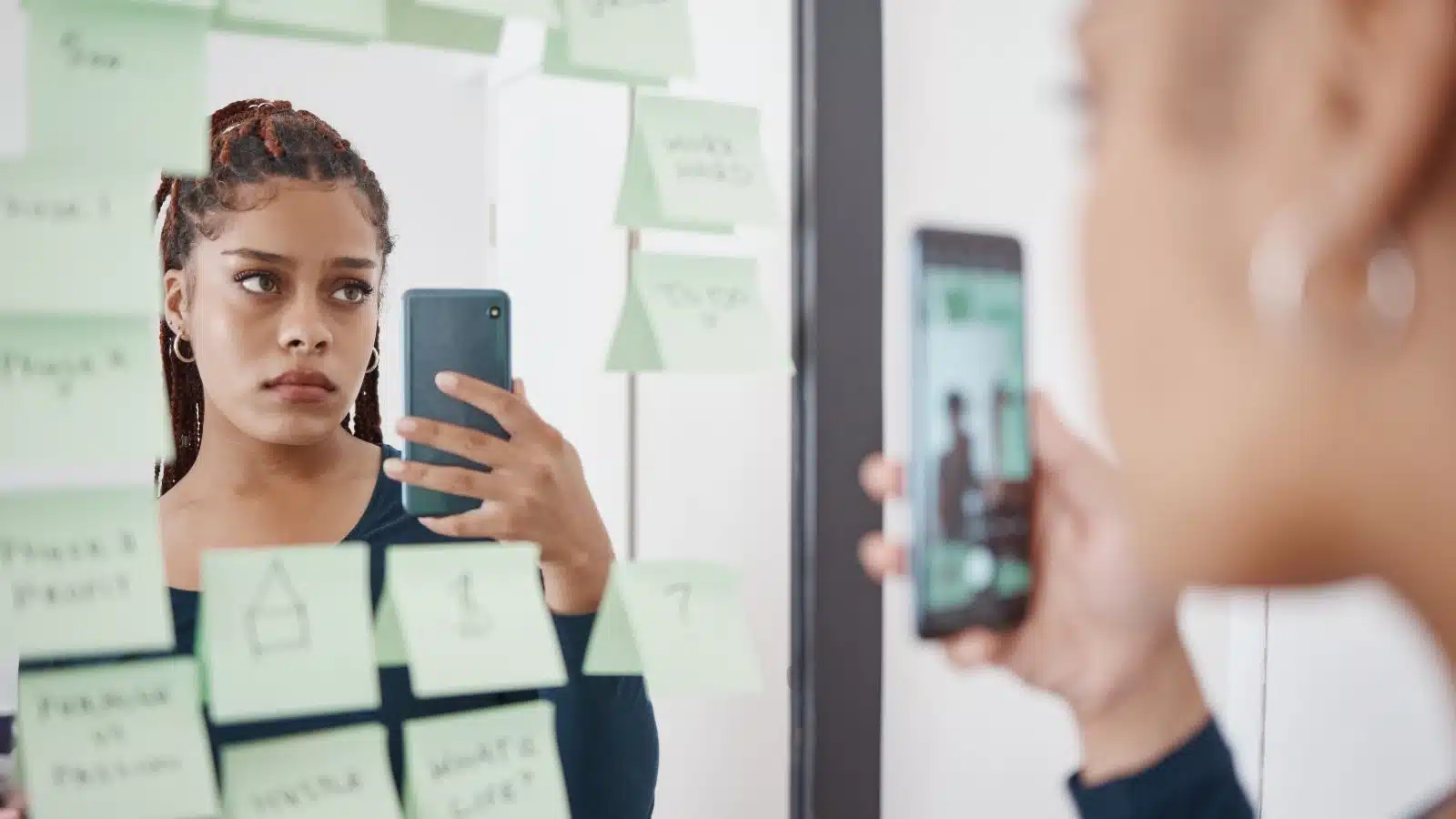 A sad, pensive looking woman struggling with self-esteem takes a selfie in a mirror filled with post it notes.