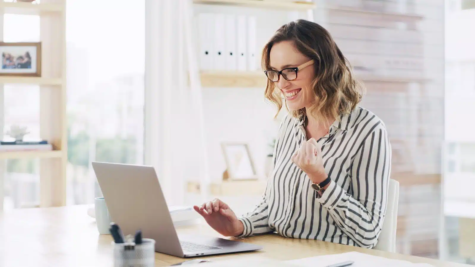 A happy woman does a fist bump at her laptop after achieving personal goals.